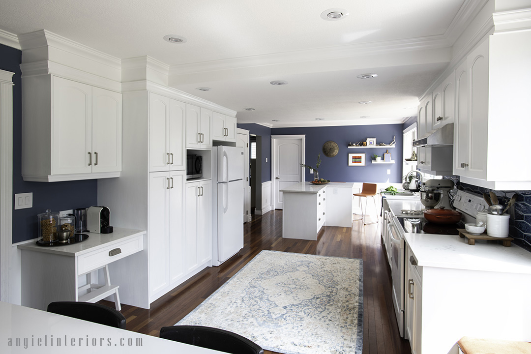 Big galley kitchen with white cabinets and appliances, navy walls and Brazilian cherry floors