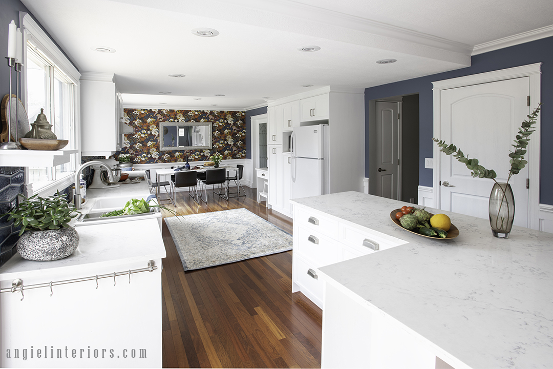White kitchen island with quartz countertop, dining area with wainscoting and bold floral wallpaper