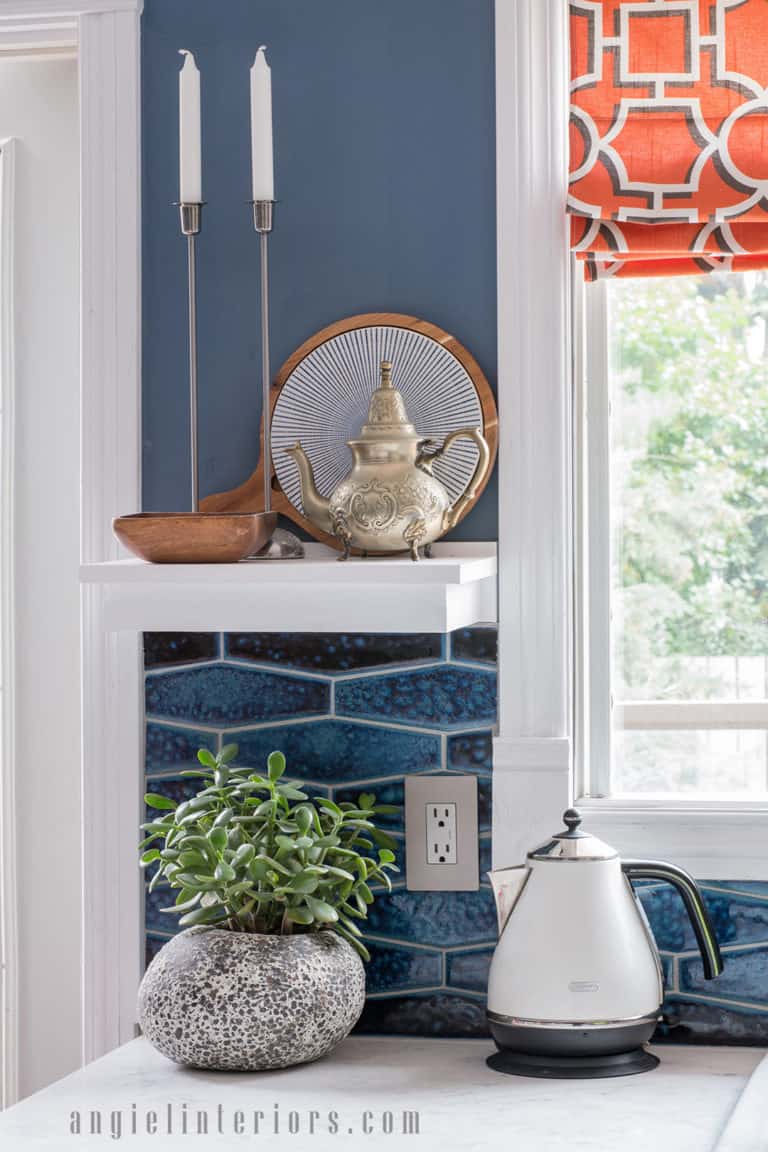 Kitchen decor details: white shelf, navy blue backsplash, orange roman shades and DeLonghi Icona kettle