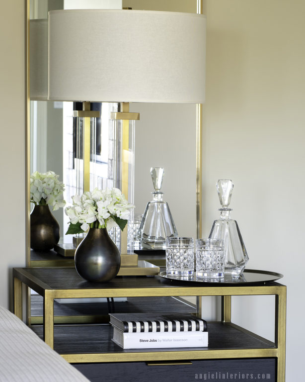 Gold and brown nightstand with gold Restoration Hardware table lamp, tray with water carafe and bronze vase with hydrangeas