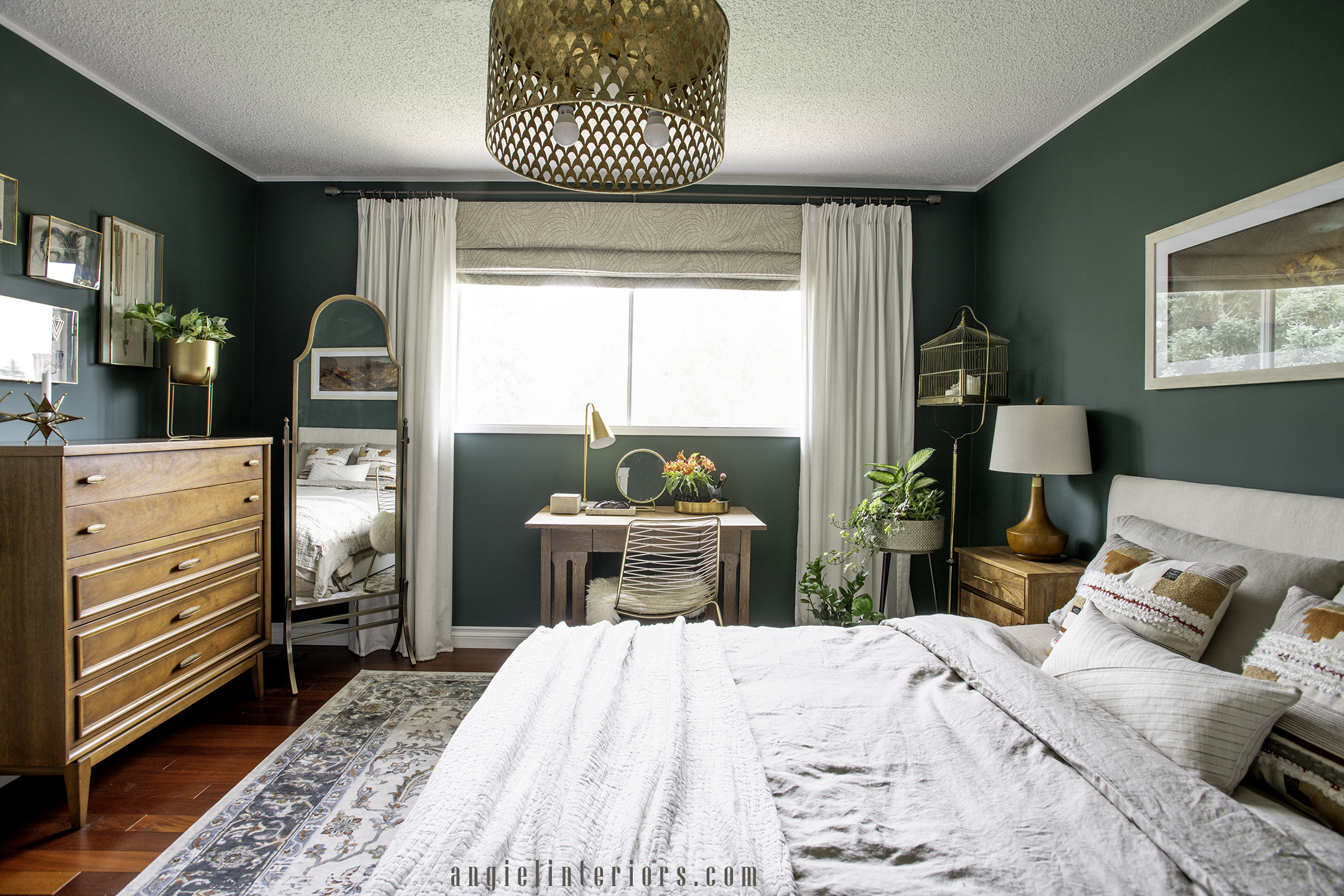 roman shades combined with pleated curtains on a brass rod in a dark green bedroom with mid century modern dresser, standing mirror, wooden vanity and nightstands