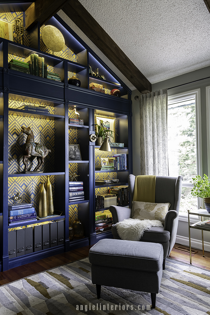 Grey IKEA Strandmon armchair with footstool in front of blue bookcase with golden Art Deco stencil and LED lights