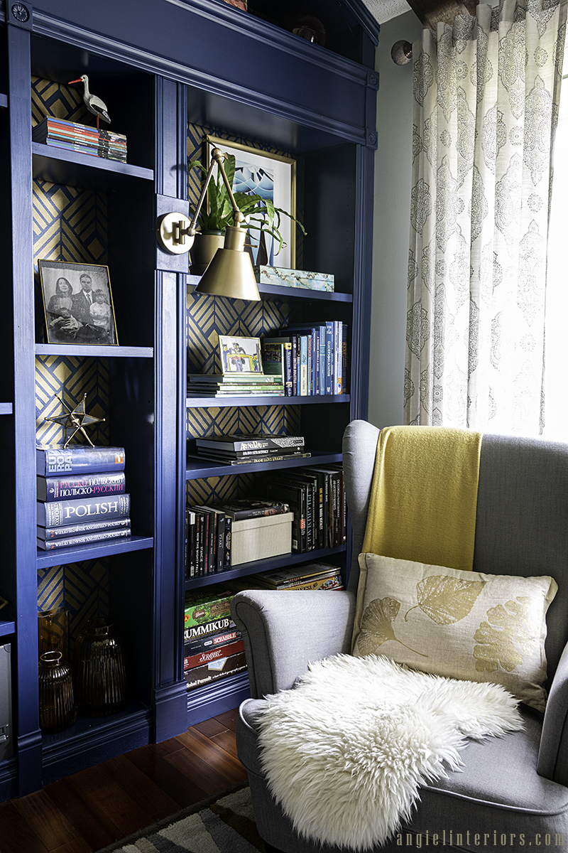 Grey IKEA Strandmon armchair with footstool in front of blue bookcase with golden Art Deco stencil